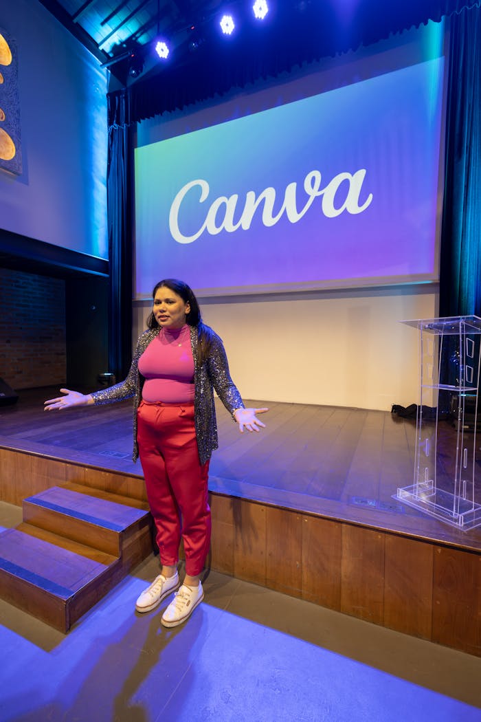Woman speaking at Canva event on stage with bright lighting.